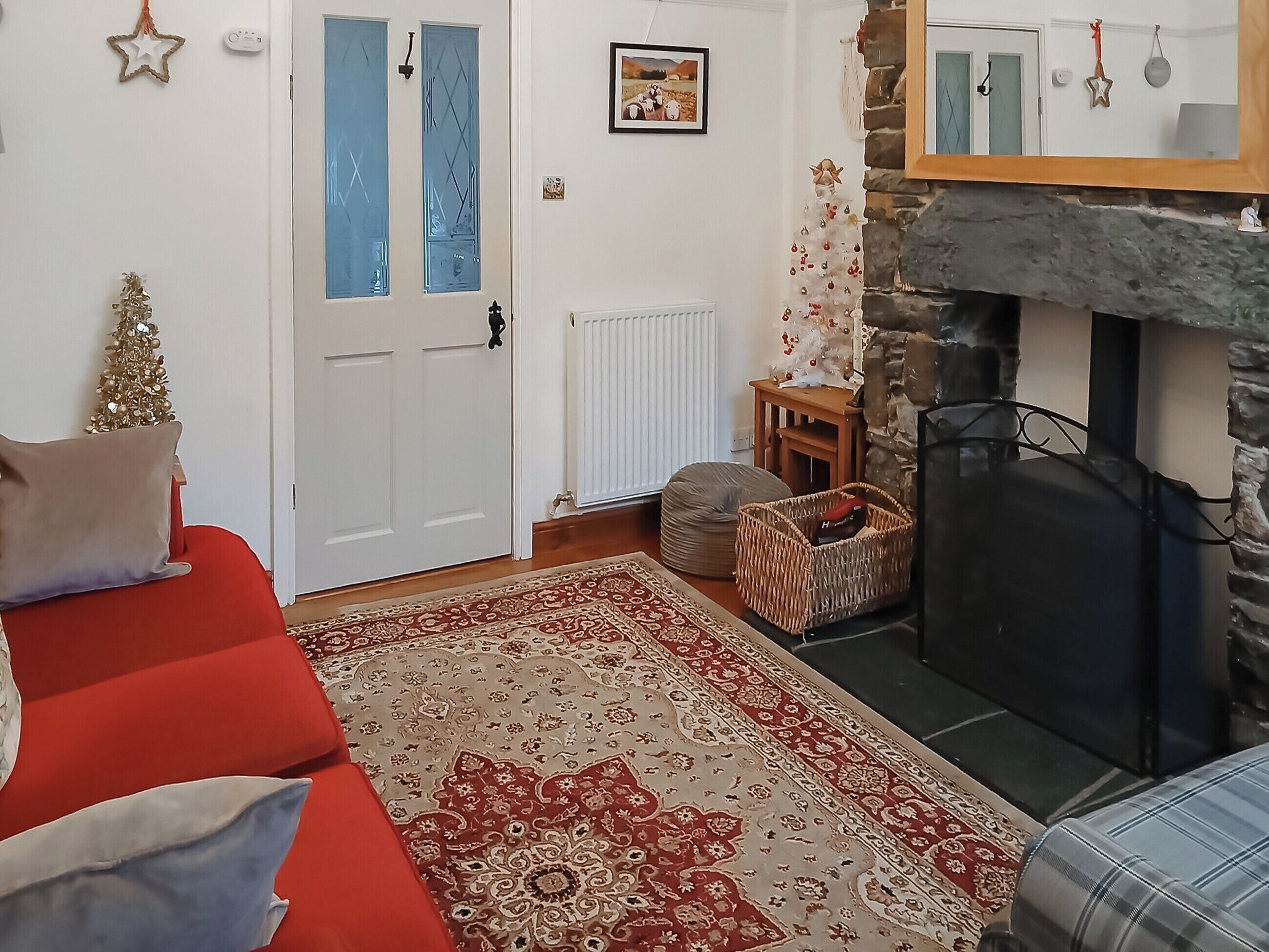 A cozy living room with a red sofa, a patterned rug, a fireplace, and a Christmas tree.
