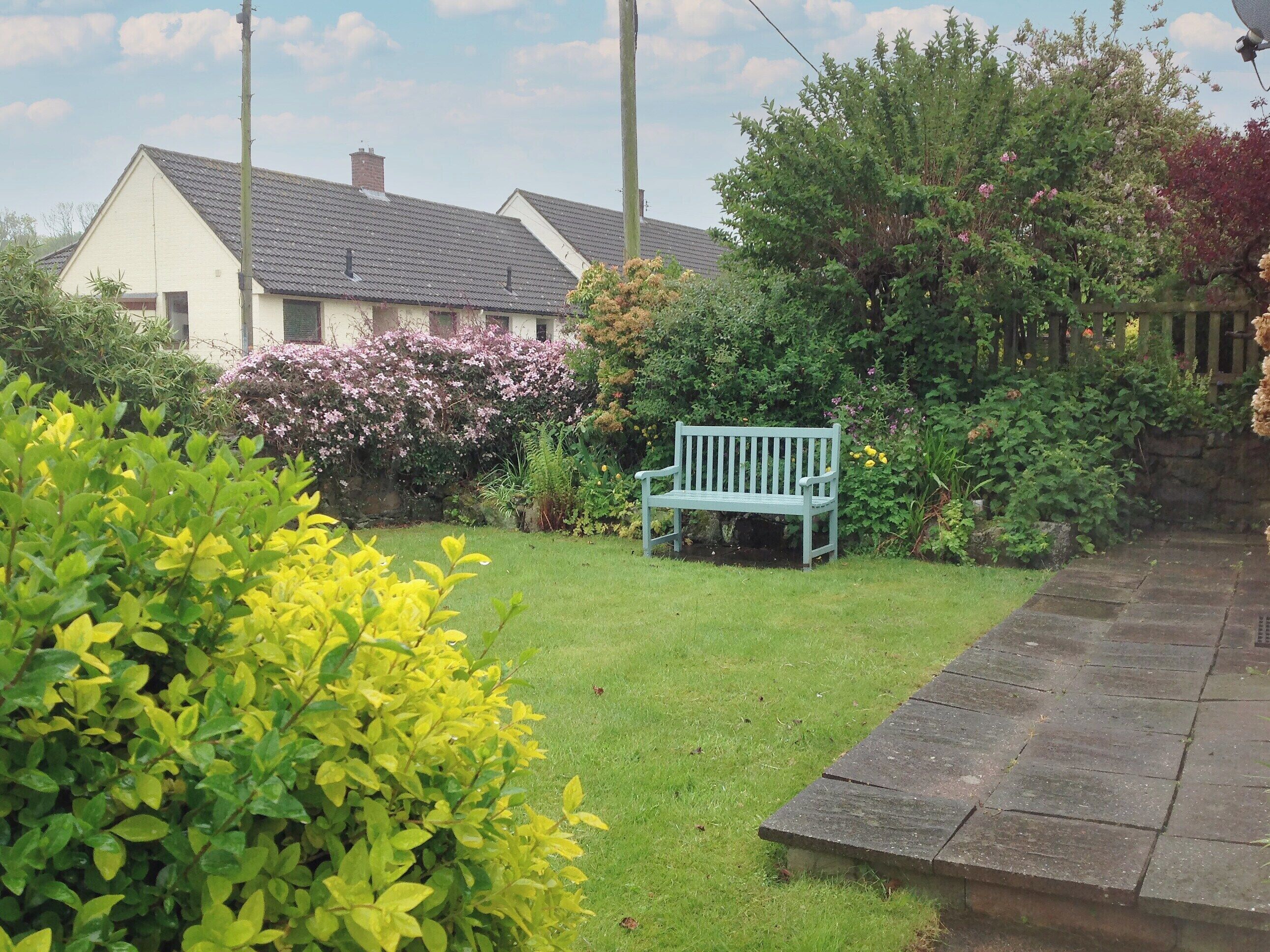 A garden with a bench, a house, and a stone pathway.