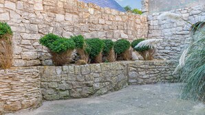 A stone wall with a small garden area, including a paved path and trimmed bushes. - 3 bedroom accommodation in Portland (Portland)