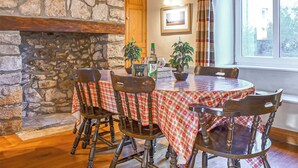 A dining area with a stone fireplace, wooden beams, and a table set with a checkered tablecloth. - 3 bedroom accommodation in Portland (Portland)