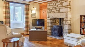 A cozy living room with a stone fireplace, wooden beams, a television, and a comfortable sofa. - 3 bedroom accommodation in Portland (Portland)