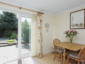 A dining area with a table and chairs, a vase of flowers, and a view of the garden through a glass door. - 3 bedroom accommodation in Weybourne, near Holt (Weybourne, near Holt)