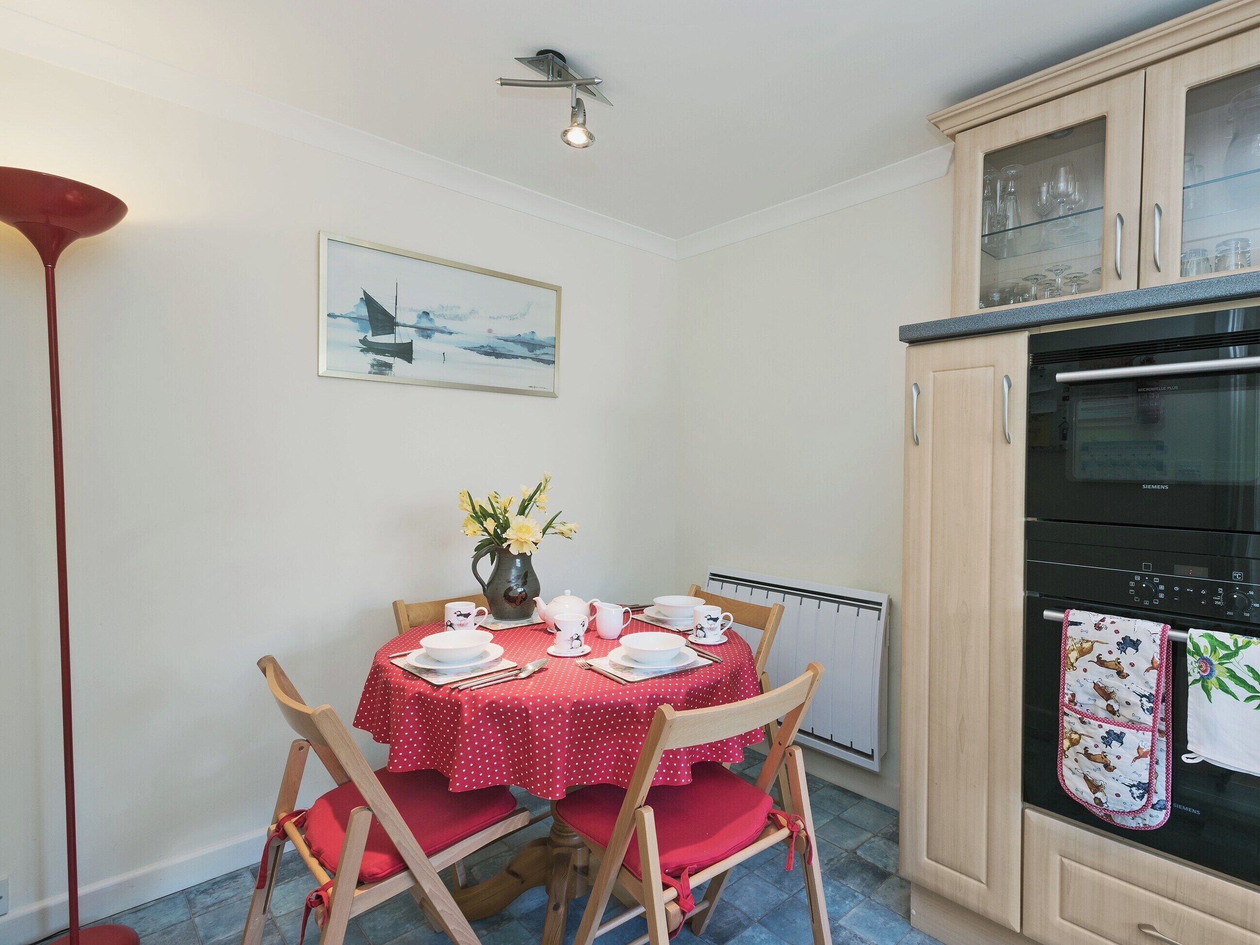 A dining area with a table set for four, chairs, a vase with flowers, and a Siemens oven.