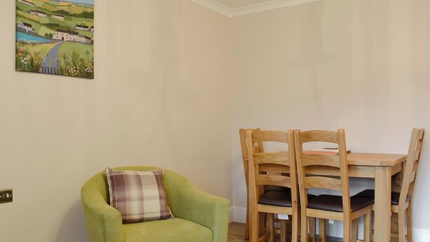 A room with a green armchair, a wooden dining table with chairs, and a landscape painting on the wall. - James' Retreat (was12 Elm Court) (Keswick)