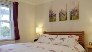 A bedroom with a bed, a nightstand, a lamp, a window with curtains, and two wall-mounted paintings. - James' Retreat (was12 Elm Court) (Keswick)