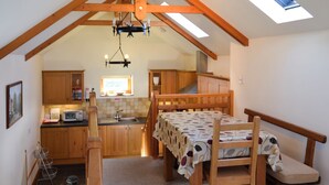 A cozy attic bedroom with a sloped ceiling, wooden beams, a skylight, a bed with a patterned bedspread, a small kitchenette, and a dining table with chairs. - 1 bedroom accommodation in Port Isaac (Port Isaac)