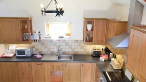 A modern kitchen with wooden cabinets, a black countertop, a microwave, a sink, a stove, and a chandelier. - 1 bedroom accommodation in Port Isaac (Port Isaac)