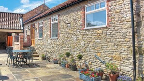 A stone building with a tiled roof, a patio with a table and chairs, and potted plants. - 2 bedroom accommodation in Kennythorpe near Malton (Kennythorpe near Malton)