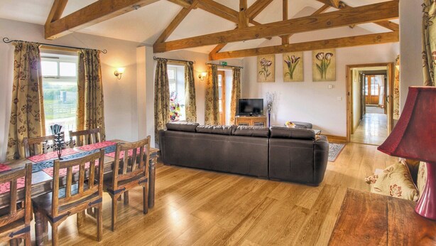 A spacious living area with wooden beams, a sofa, a TV, and a dining table with chairs. - 2 bedroom accommodation in Kennythorpe near Malton (Kennythorpe near Malton)