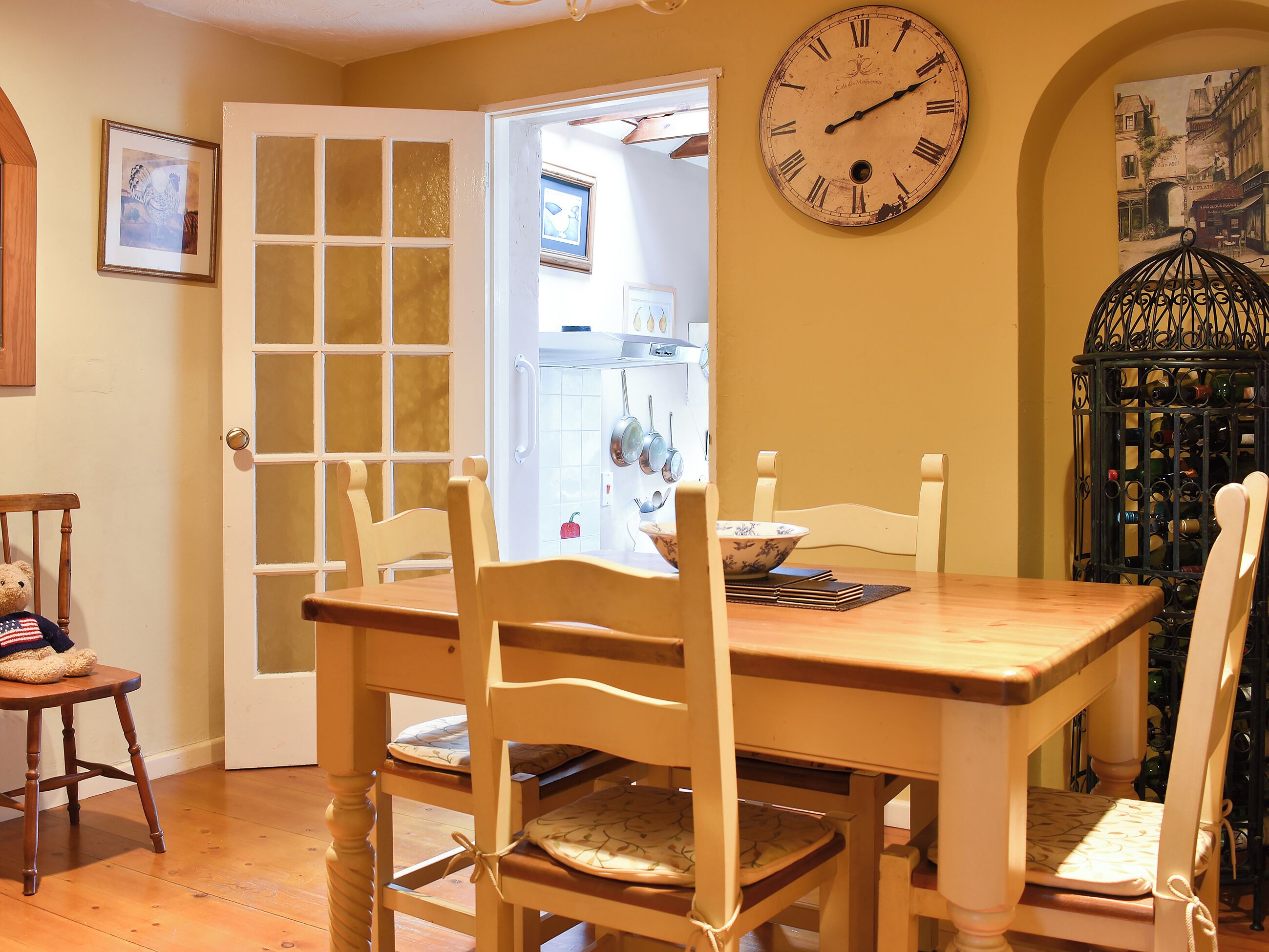 Un comedor con una mesa y sillas de madera, un reloj de pared y una estantería para vinos.