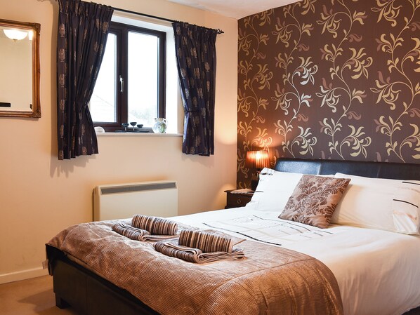 A neatly made bed with a striped blanket, a bedside lamp, and a floral wallpaper pattern.