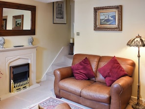 A living room with a brown leather sofa, two red cushions, a fireplace, a framed picture on the wall, and a floor lamp. - 2 bedroom accommodation in Cerne Abbas, near Dorchester (Cerne Abbas, near Dorchester)