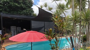 A swimming pool with a red umbrella, surrounded by metal railings and tropical plants. - Close to amenities, NBN, Swimming pool, Netflix,  (Kirwan)
