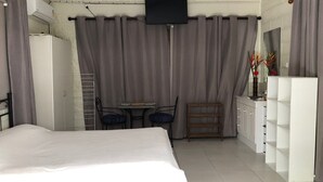 A hotel room with a bed, a TV mounted on the wall, a small table with chairs, a vanity with a mirror, and a cabinet with shelves. - Close to amenities, NBN, Swimming pool, Netflix,  (Kirwan)