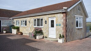 A stone building with a tiled roof, a white door, and a small garden area with potted plants.