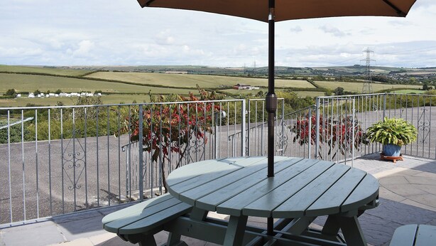 A patio with a table and an umbrella, overlooking a rural landscape with fields and a distant village.