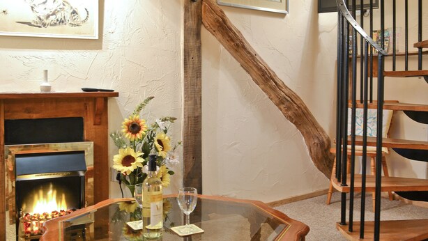 A living room with a glass-top coffee table, a fireplace, a wooden staircase, and a framed picture on the wall. - Byre Cottage - 29410 (Stelling Minnis, near Canterbury)