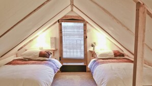A cozy attic bedroom with two beds, a window with blinds, and a small table with a lamp. - Byre Cottage - 29410 (Stelling Minnis, near Canterbury)