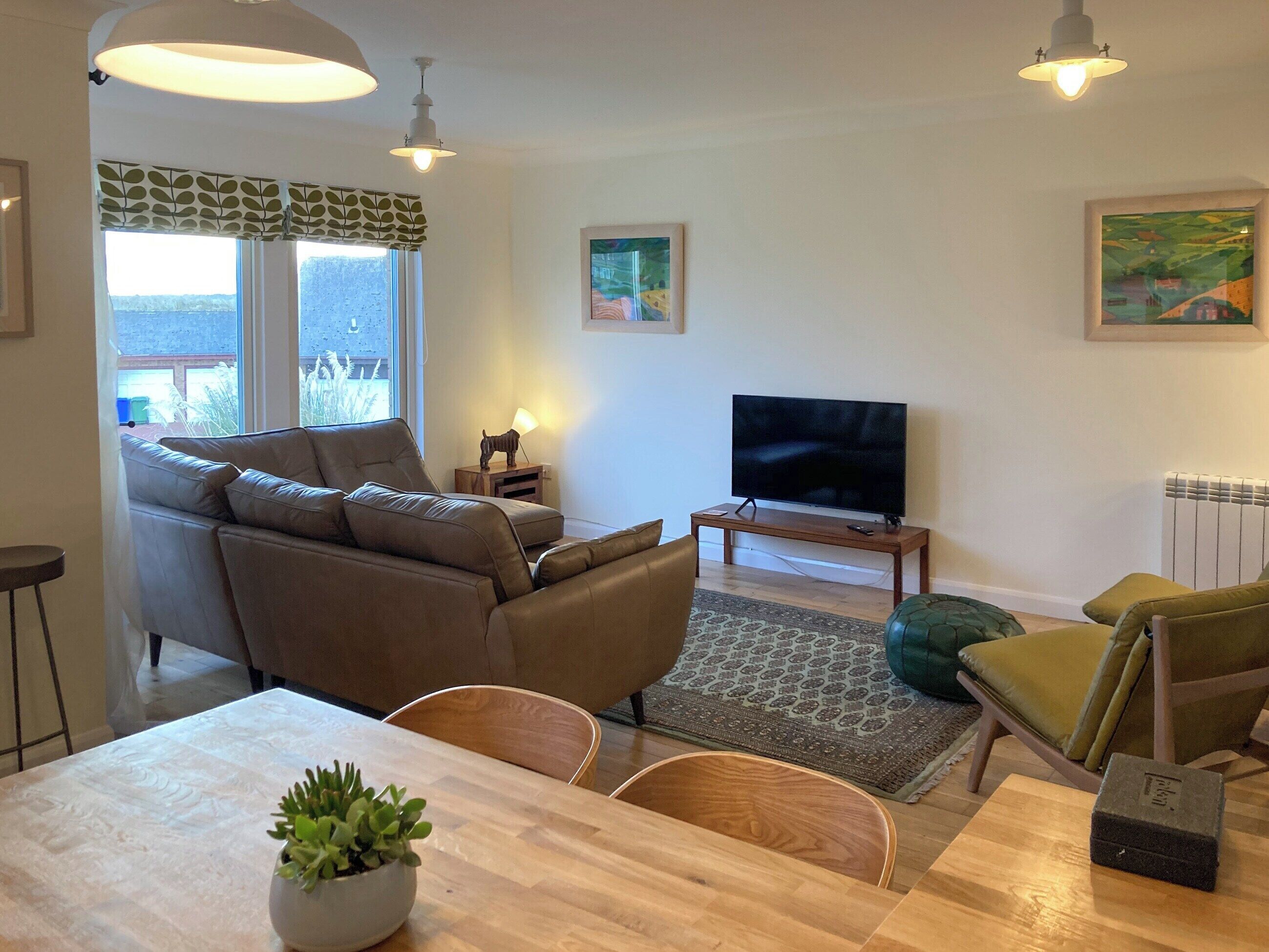 Una sala de estar con sofá, televisión, mesa de comedor, sillas y una planta en maceta.
