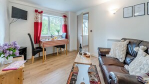 Un salon avec un canapé en cuir marron, une table à manger recouverte d’une nappe à carreaux et un téléviseur fixé au mur.