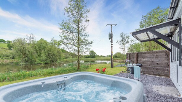 Un bain à remous avec vue sur un lac, entouré d’une clôture en bois et d’une zone herbeuse.