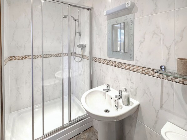 Un baño moderno con cabina de ducha de vidrio, un lavamanos blanco con un espejo encima y un salpicadero de azulejos.