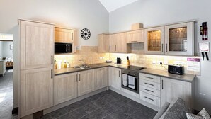 Una cocina moderna con armarios de madera clara, un microondas negro, un lavamanos de acero inoxidable y un horno integrado.