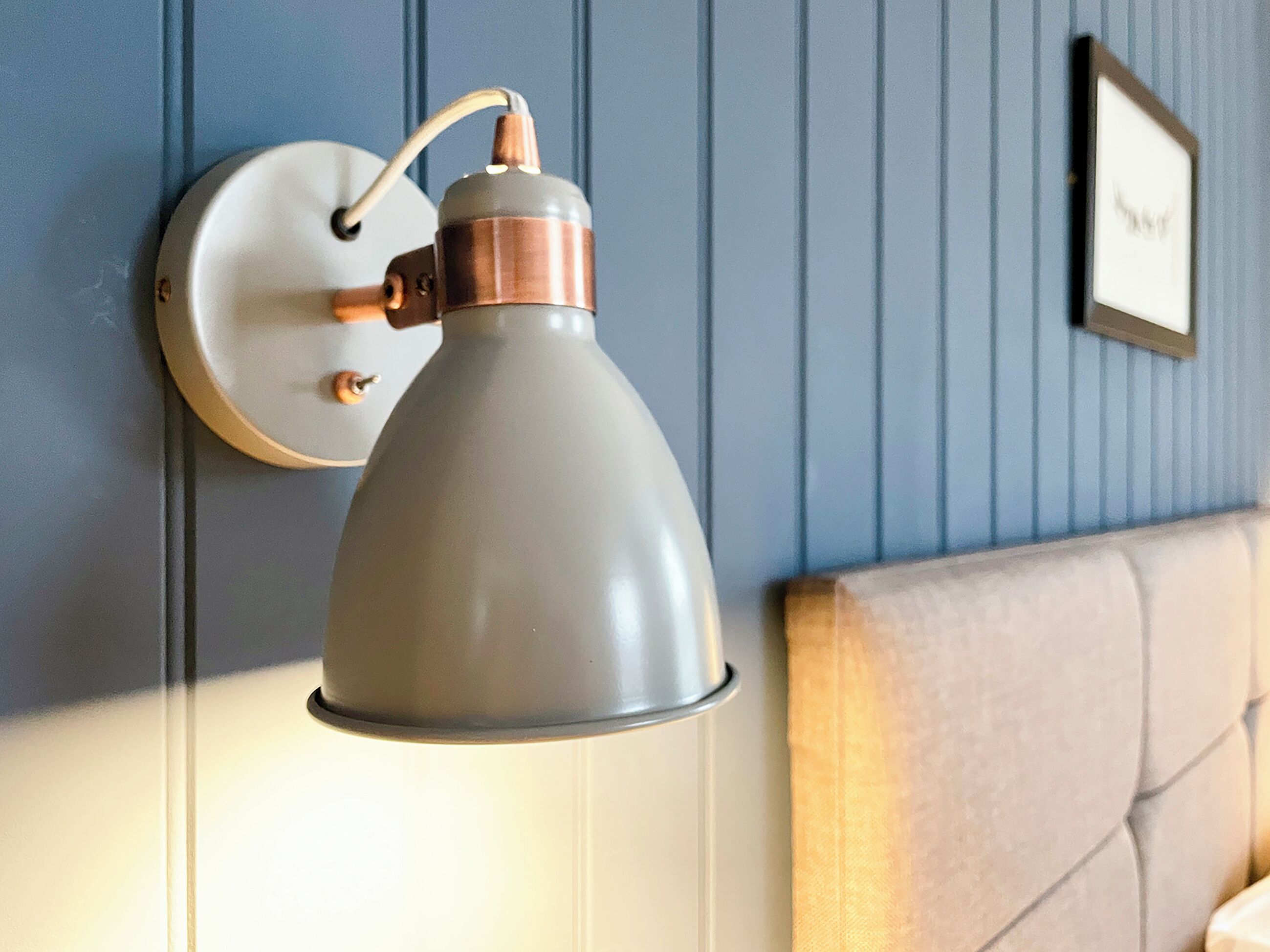 A wall-mounted lamp with a copper base and a white shade, mounted on a blue paneled wall.