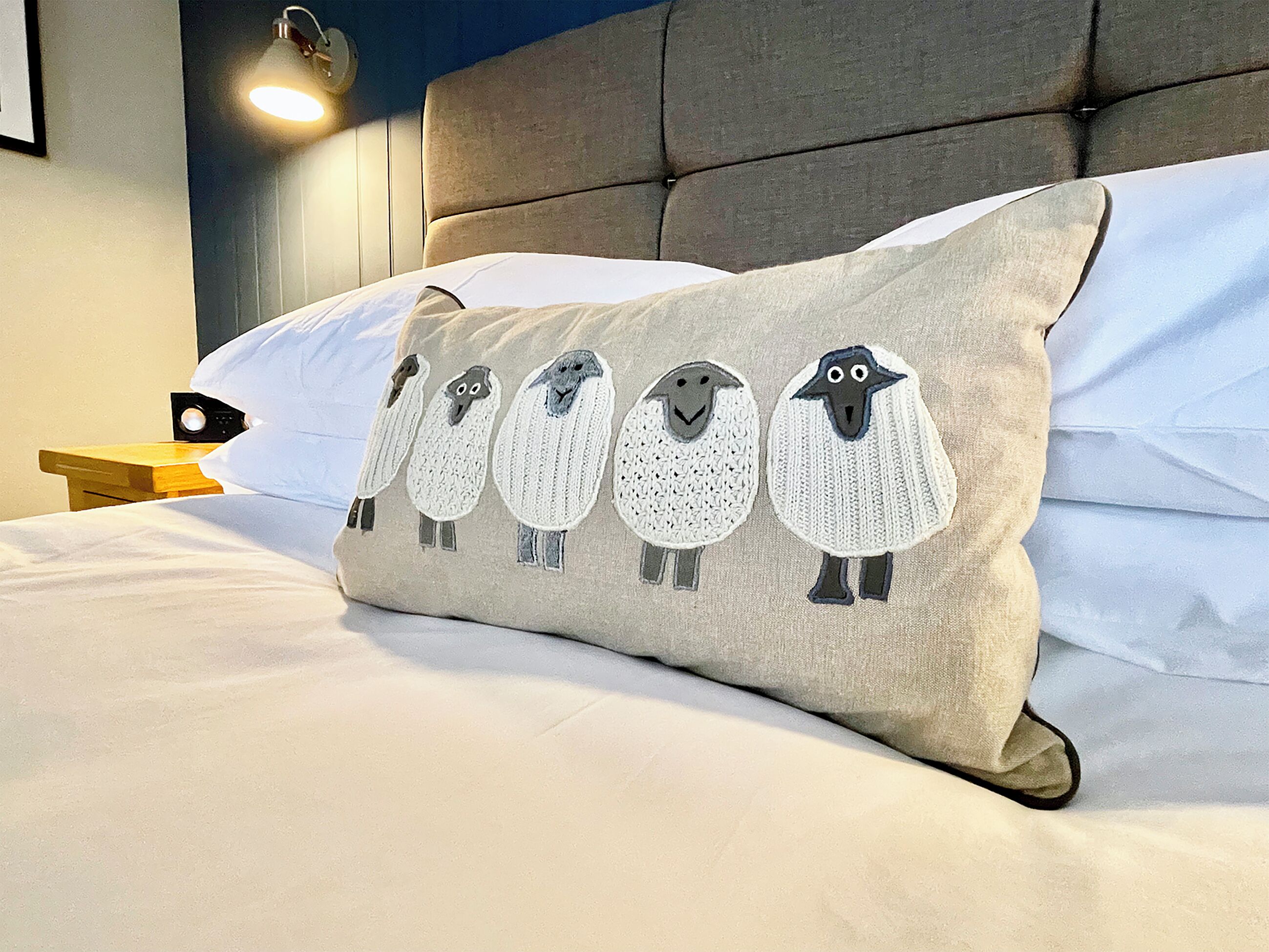 A bed with a pillow featuring a knitted sheep design.