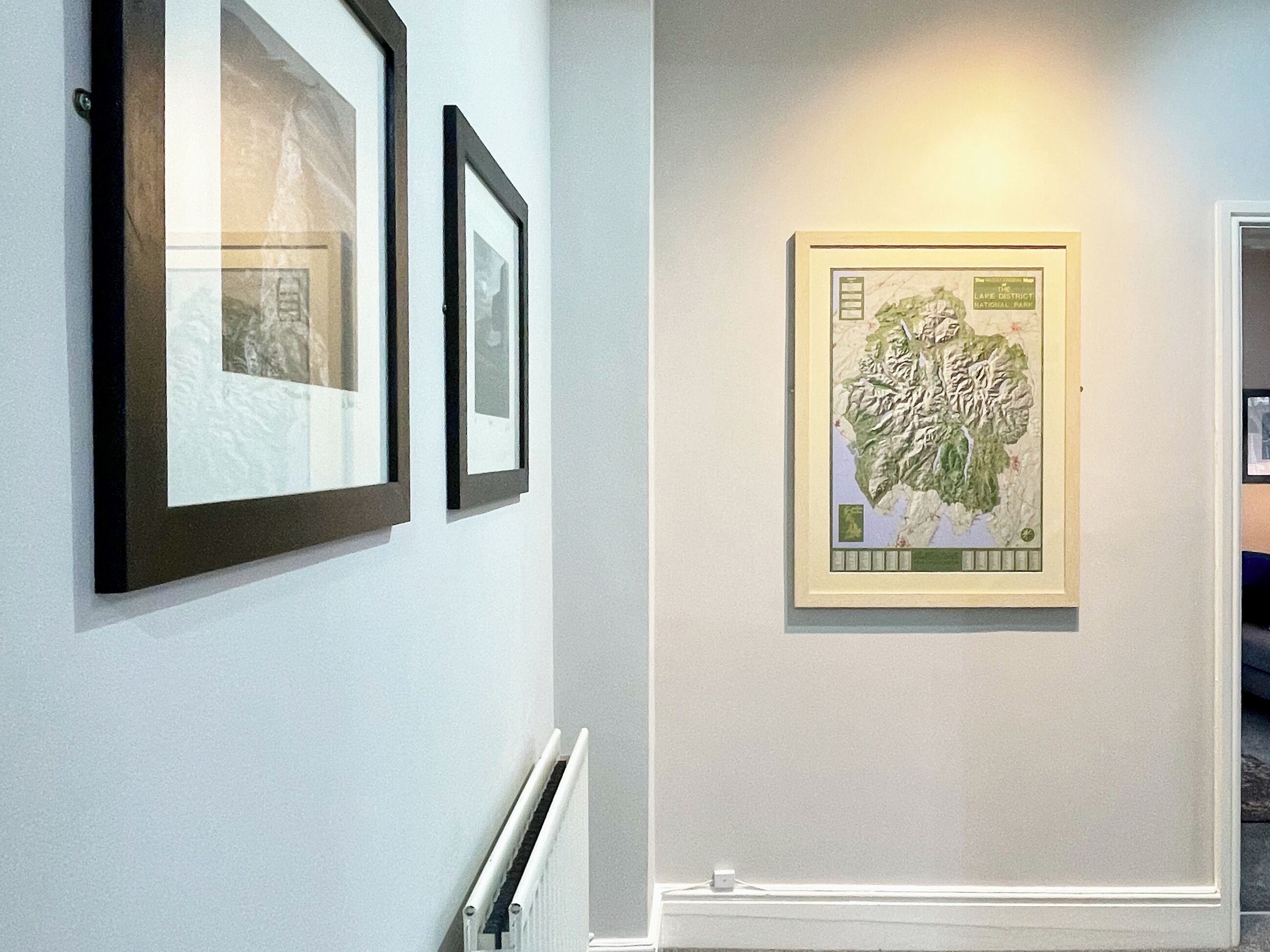 A hallway with framed photographs on the left and a map on the right.