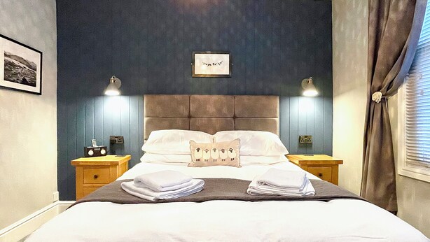 A neatly made bed with a pillow featuring owls, two bedside lamps, and a framed picture on the wall. - High Style Apartment (Keswick)