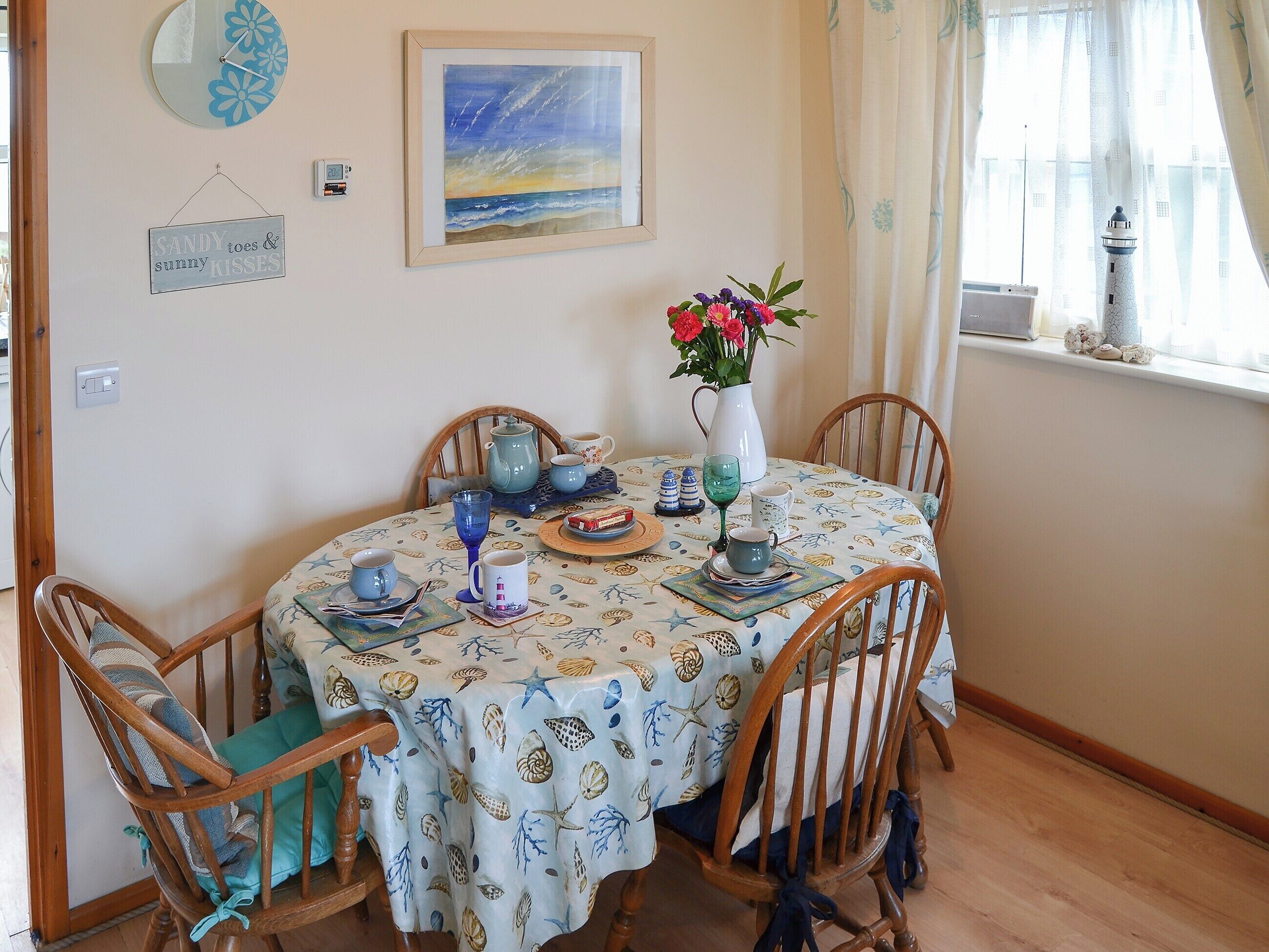 A dining table with a seashell tablecloth, surrounded by wooden chairs.