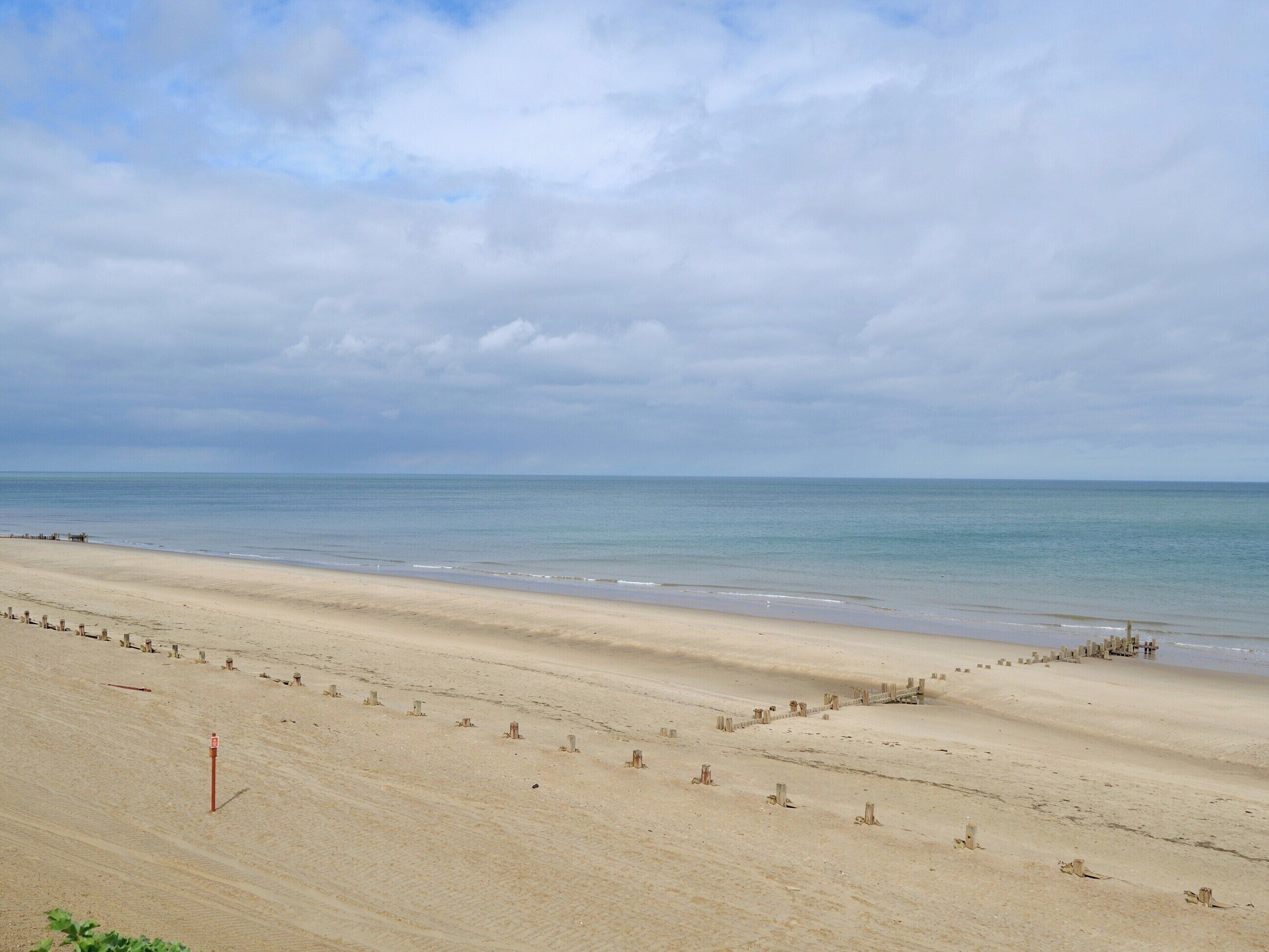 Una extensa playa de arena con un mar tranquilo bajo un cielo nublado.