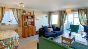 A cozy living room with a blue sofa, a green armchair, a wooden cabinet with books, and a dining table with chairs. - 2 bedroom accommodation in Walcott (Walcott)