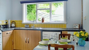Une cuisine avec une fenêtre, des placards en bois, un évier et un coin repas avec une table mise pour deux personnes.
