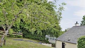 Une maison avec un toit en pente, un petit porche et un jardin avec un arbre et de la pelouse.