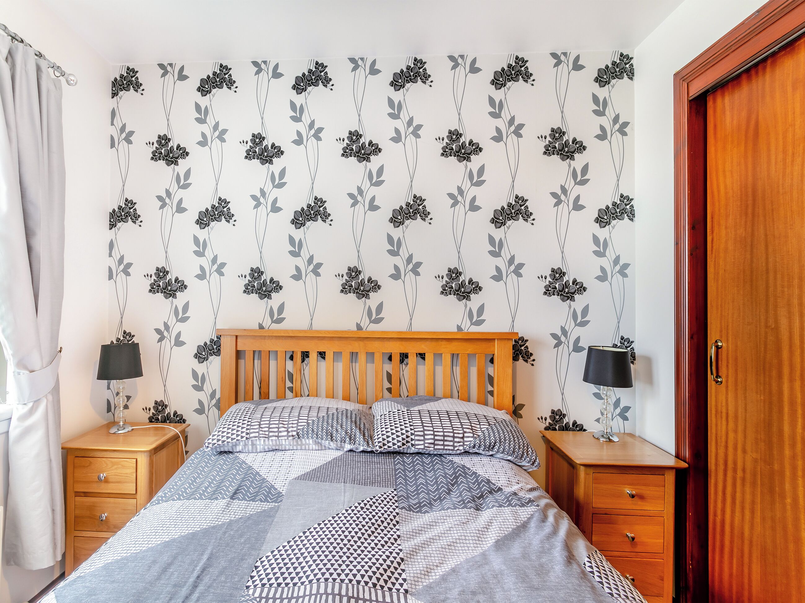 Une chambre à coucher avec un lit en bois, deux tables de chevet, une commode et une porte.