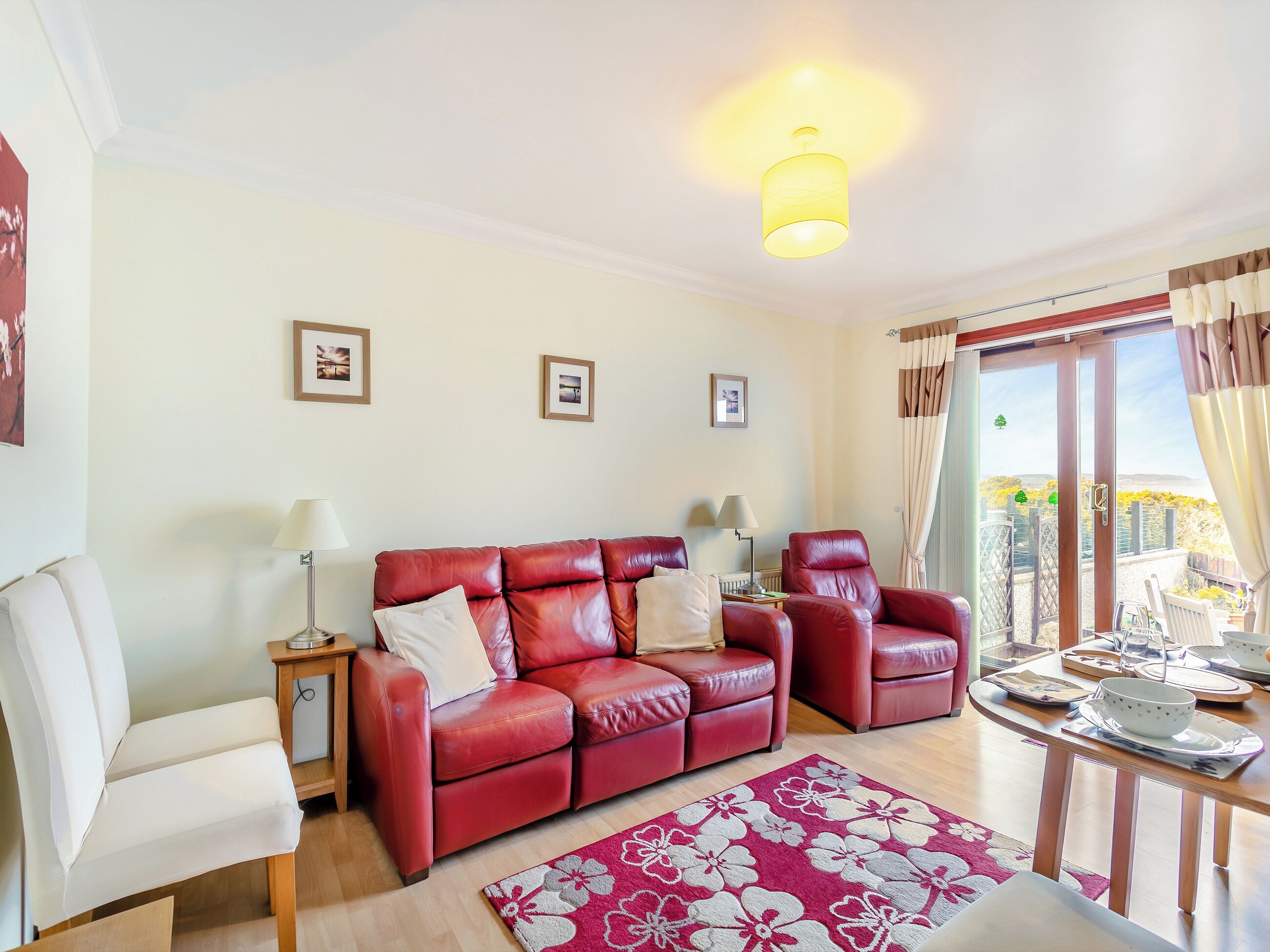 A living room with a red leather sofa, two armchairs, a wooden coffee table, and a balcony with a view.