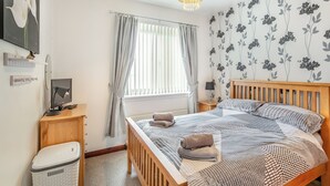 Et soveværelse med en træseng, et sengebord med lampe, et vægmonteret fjernsyn og et vindue med gardiner.