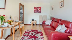 En stue med en rød lædersofa, et spisebord med stole, et lille sofabord og en blomstret måtte.