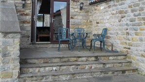 Un bâtiment en pierre avec un toit recouvert de tuiles rouges, un banc en bois et une table avec deux chaises.