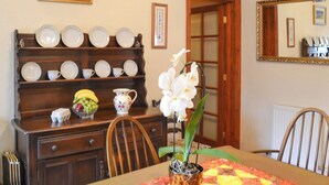 Un coin repas avec un buffet en bois, une table recouverte d’une courtepointe, un pot d’orchidée et un panier de fruits.