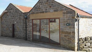Un bâtiment en pierre avec un toit en tuiles, une grande porte vitrée et un panneau indiquant la présence d’un nid d’oiseau.