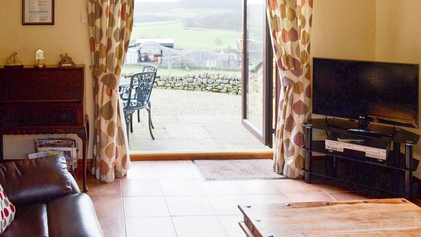 Un salon avec un téléviseur, un canapé et une table. Il y a une fenêtre avec des rideaux et une vue sur l’extérieur.