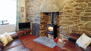 Una sala de estar acogedora con pared de piedra, chimenea, sofás de cuero y televisor.