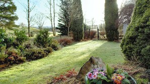 Un jardín con césped, diversas arbustos y una gran roca.