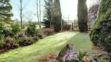 A garden with a grassy lawn, a variety of shrubs, and a large rock.