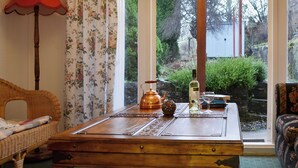 Una habitación con una mesa de madera, una silla de mimbre, una lámpara roja y vistas a zonas verdes al exterior.
