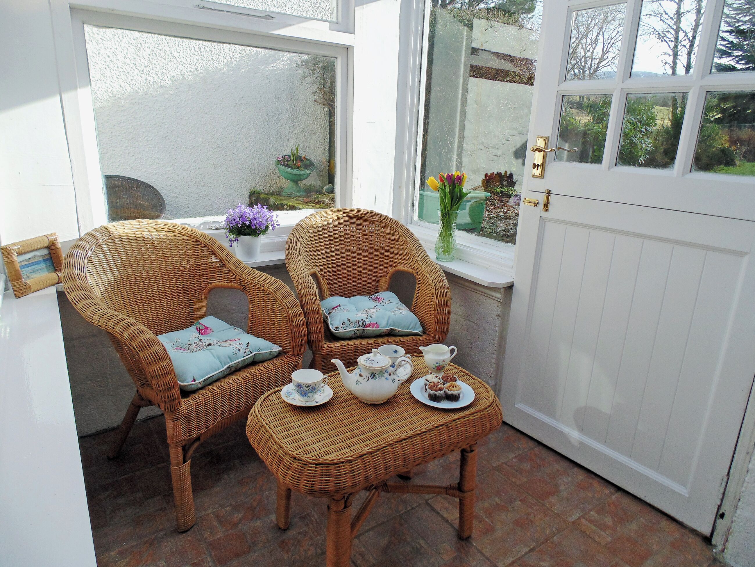 A room with two wicker chairs, a small table with tea set, and a white door.