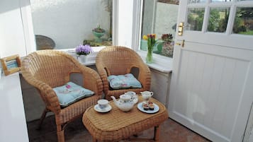 A room with two wicker chairs, a small table with tea set, and a white door.